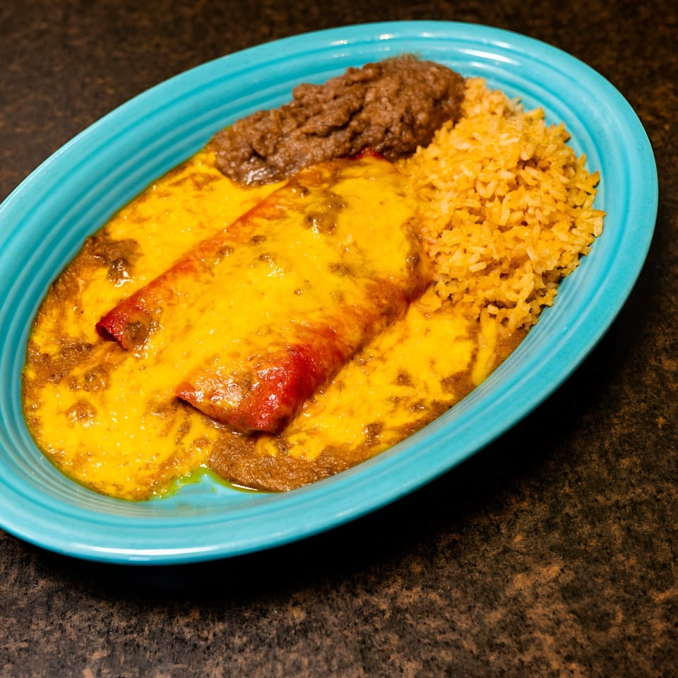 Two cheesy enchiladas with rice and refried beans on a blue oval plate.