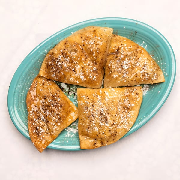 Four golden-brown sopapillas, drizzled with honey and sprinkled with powdered sugar, on a blue plate.