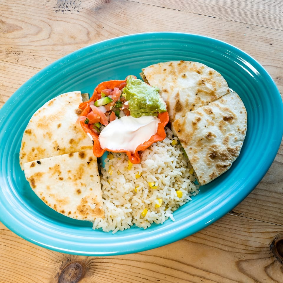 El Chaparral quesadillas, rice, guacamole, salsa, and sour cream on a blue plate.