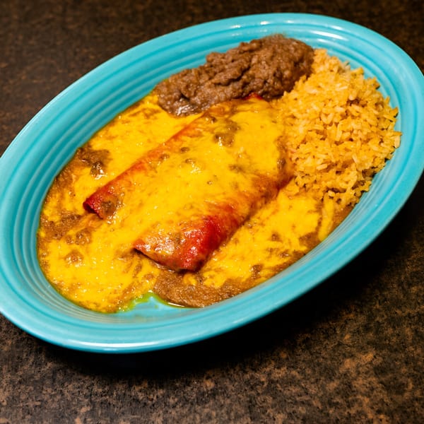 Two enchiladas covered in melted cheese and sauce, with refried beans and rice on a blue plate.