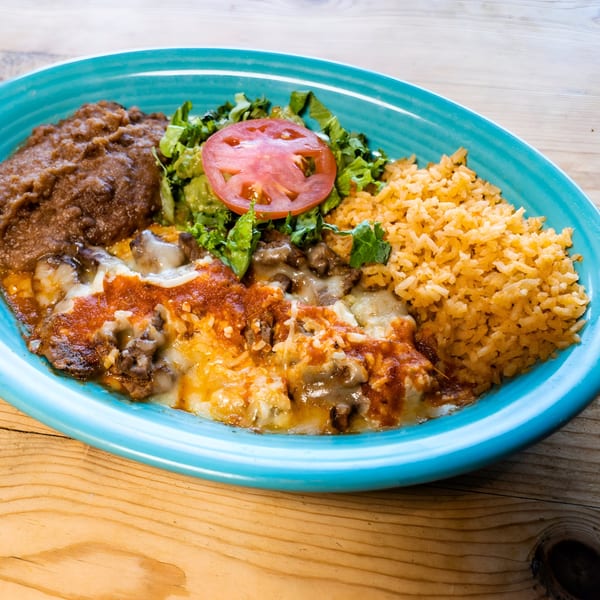 A vibrant blue plate holds a Mexican dish with refried beans, rice, salad, and cheesy meat.