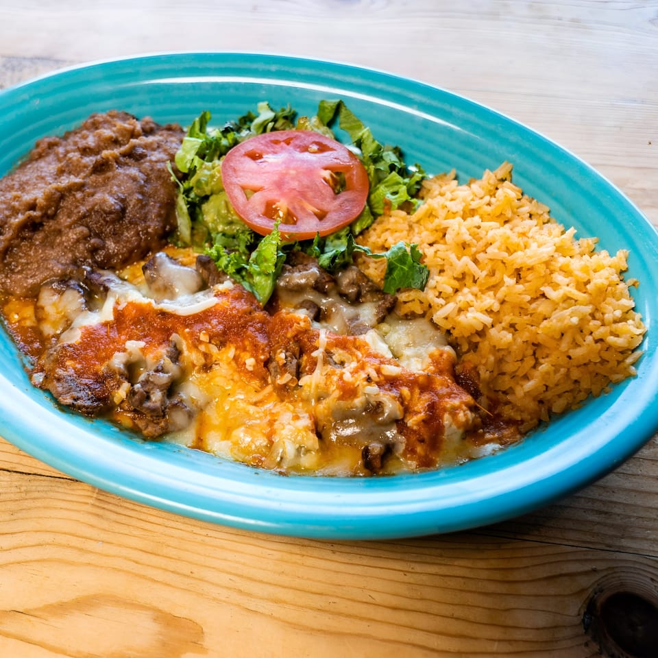 A vibrant blue plate holds a Mexican dish with refried beans, rice, salad, and cheesy meat.