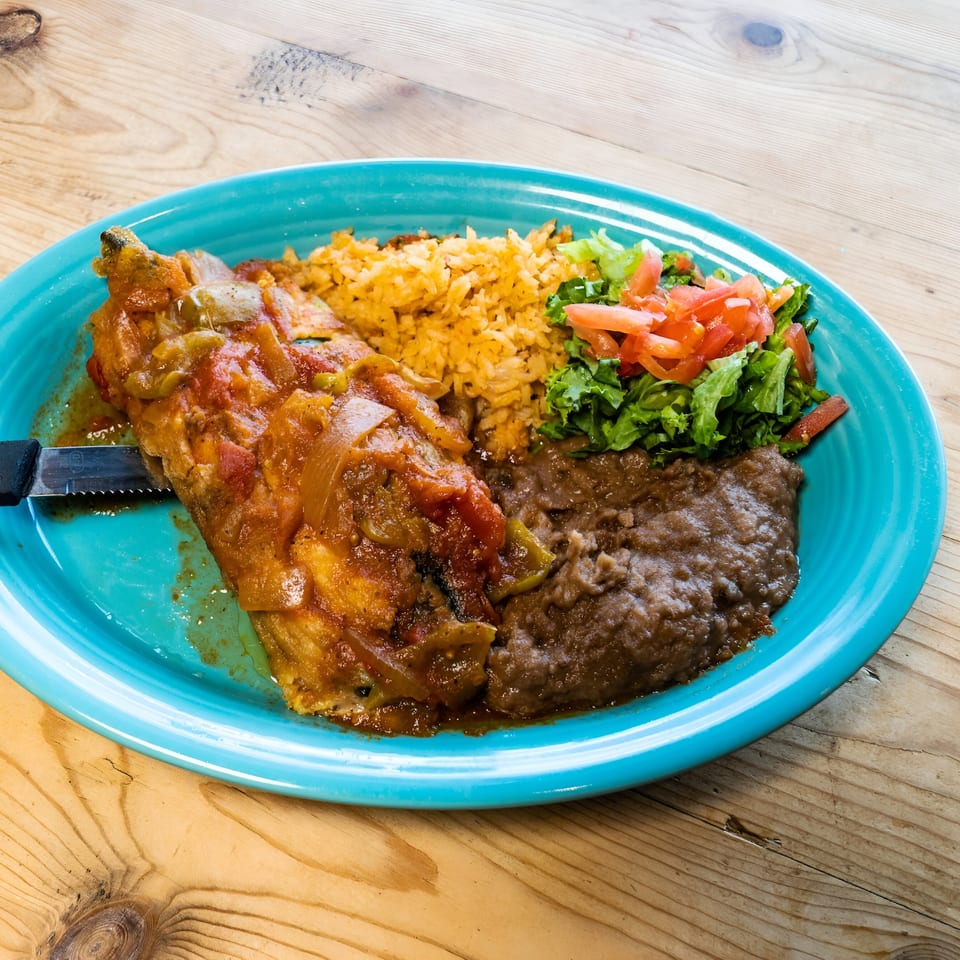 El Chaparral's Mexican dish with chile relleno, rice, refried beans, and a side salad on a blue plate.